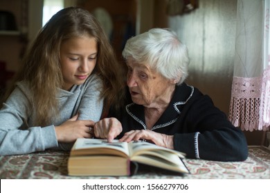 Cute Teen Girl With Her Old Great-grandmother Reading A Book.