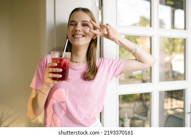 Cute teen girl holding a glass of juice and smiling at the camera. Smiling brunette in a pink t-shirt drinking lemonade posing and laughing