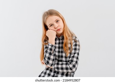 Cute Teen Girl Looks Bored Or Upset, Sulks With Head On Fist, Stands Disappointed Against White Background, Wears Casual Clothes