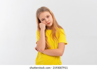 Cute Teen Girl Looks Bored Or Upset, Sulks With Head On Fist, Stands Disappointed Against In Blank Yellow Tshirt Over White Background