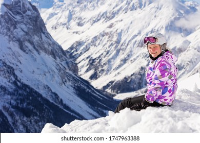 Cute Teen Girl Sit In Snow On Top Of The Mountain In Ski Outfit With Helmet And Mask Turn Back Smiling To Camera