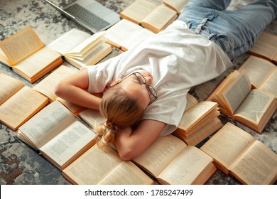 Cute teen girl student in casual clothing and glasses lying on books after holidays, back to school, exam preparation
