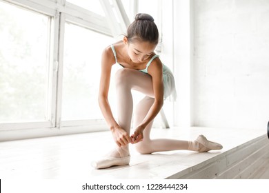 Cute Teen Girl Tying Ballet Shoes By The Big Window