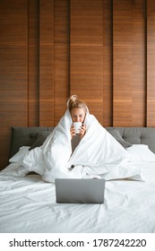 Cute Teen Girl Under Blanket In White Bed In Bedroom Woken Up And Drink Tea With Laptop. Breakfast In Bed, Lazy Morning