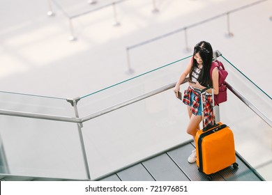 Cute Teenage Asian Traveler Girl, College Student Using Smartphone Call Or Chat At Airport With Luggage, Backpack. Web Check In, Lonely Travel Study Abroad, Or International Tourism Lifestyle Concept.