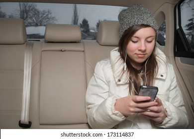 Cute Teenage Girl With Hat And Earbuds In Backseat Of Car