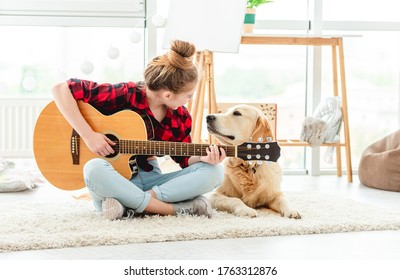 Cute teenage girl playing guitar with lovely dog indoors