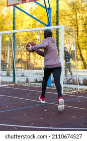 Cute Teenager In A Hoodie Playing Basketball. Young Boy With Ball Learning Dribble And Shooting On The City Court. Hobby For Kids, Active Lifestyle	