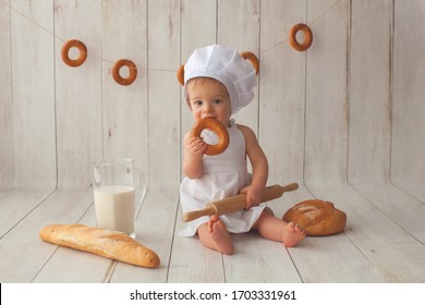 Der zehn Monate alte kleine Junge sitzt in einem Anzug eines Kochs auf hellhölzernem Hintergrund.  Kochmütze auf dem Kopf. Er ist Bäckereikoch.