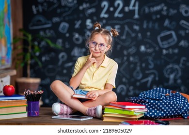 Cute Thoughtful Tired Schoolgirl With Glasses. Sitting At His Desk At Home And Bored. Back To School. Little Girl C Does Not Want To Get Knowledge And Do Homework. Learning Problems