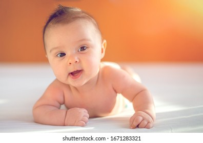 Cute three months old Baby girl infant on a bed on her belly with head up looking into camera with her big eyes. Natural bedroom light.