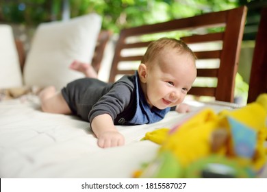 Cute three months old baby boy playing with his colourful toys outdoor. Baby during tummy time. Cute little child learning to crawl.