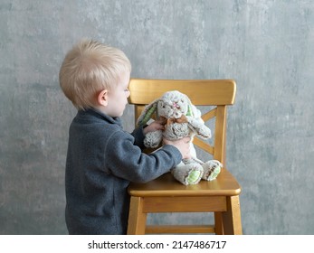 Cute Three-year Old Blond Boy Seen In Profile Placing A Stuffed Bunny Toy On A High Chair