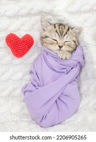 Cute Tiny Kitten Wrapped Like A Baby, Sleeps With Red Heart On A Bed. Top Down View