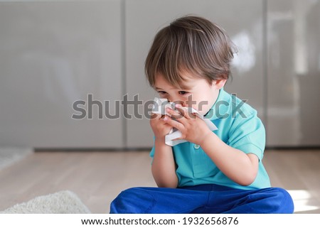 Cute toddler boy blowing nose into tissue paper at home. Mixed race Asian-German baby concept for coronavirus, Covid-19 sickness or allergy.