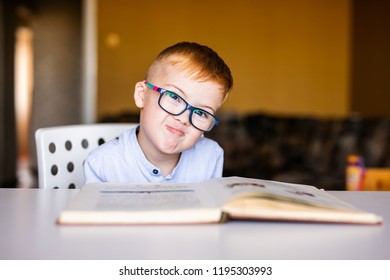 Cute toddler boy with down syndrome with big glasses reading intesting book.