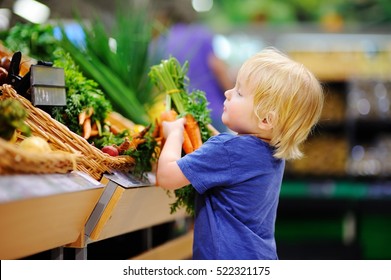 Cute Toddler Boy In A Food Store Or A Supermarket Choosing Fresh Organic Carrots. Healthy Lifestyle For Young Family With Kids