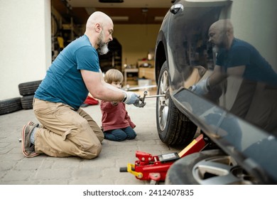 Cute toddler boy helping his father to change car wheels at their backyard. Father teaching his little son to use tools. Active parent of a small child. - Powered by Shutterstock