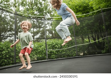 Cute toddler boy and his sister jumping on a trampoline in a backyard. Sports and exercises for children. Summer outdoor leisure activities.