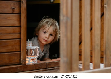 Cute toddler boy, holding lantern, hiding behind wooden door in little playhouse in garden - Powered by Shutterstock