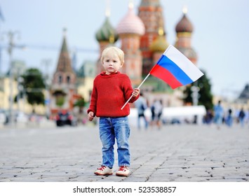Cute toddler boy holding russian flag with Red Square and Vasilevsky descent on background