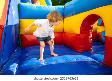 Cute toddler boy jumping on a inflatable bouncer in a backyard on warm and sunny summer day. Sports and exercises for children. Summer outdoor leisure activities. - Shutterstock ID 2318963621