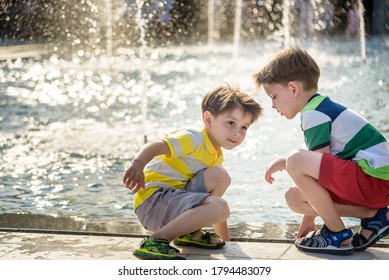 Cute toddler boy and older brother, playing on a jet fountains with water splashing around, summertime concept