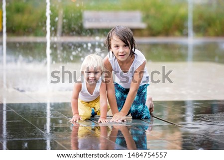 Cute toddler boy and older brothers, playing on a jet fountains with water splashing around, summertime