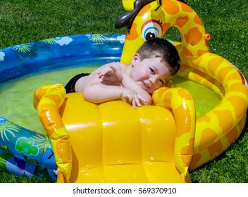 A Cute Toddler Boy Plays In A Blow Up Pool On A Hot Summer Day