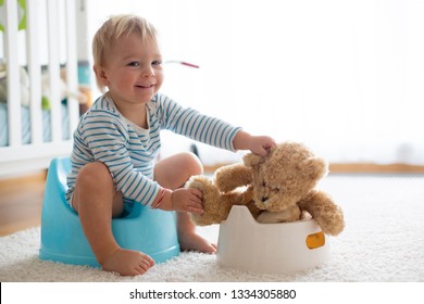Cute toddler boy, potty training, playing with his teddy bear on potty