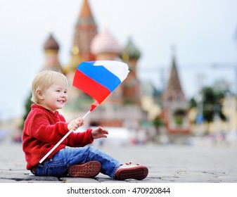 Cute toddler boy sitting and playing with russian flag with Red Square and Vasilevsky descent on background