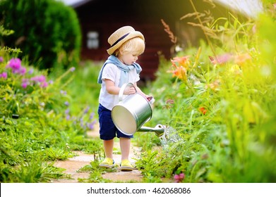 Cute toddler boy in straw hat watering plants in the garden at summer sunny day