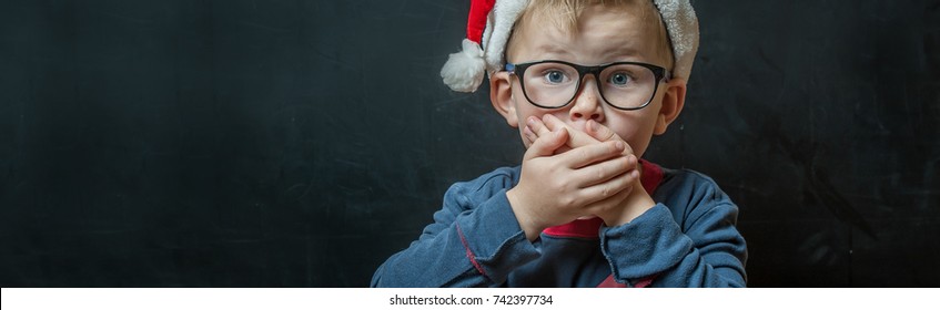 Cute Toddler Boy Suprised And So Happy About It. Christmas Magic. Child Waiting For Xmas Presents. Kid In Red Hat And Glasses.