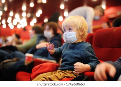 Cute toddler boy wearing face mask watching cartoon movie in the cinema. Lifting virus lockdown. Social distancing restrictions remain. Leisure or entertainment for family with kids after quarantine.