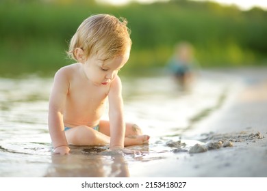 Cute toddler boy wearing swimming diaper playing by a river on hot summer day. Adorable child having fun outdoors during summer vacations. Water activities for kids.