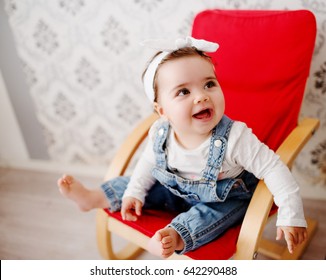 Cute toddler in a chair, posing and smiling. Baby girl wearing denim and a hair bun.