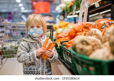 Cute toddler child, boy, wearing medical mask in supermarket store during covid pandemic lockdown