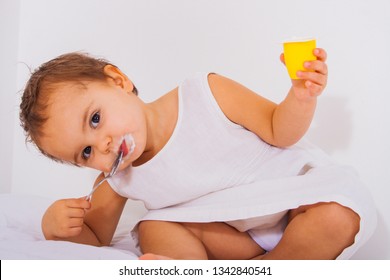 Cute Toddler Eating Some Yoghurt In A White Dress