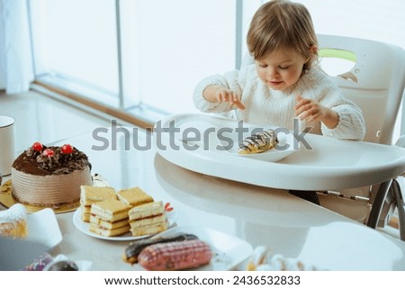 Cute toddler eats eclair with chocolate, harm from sugar to the health of a child, tooth problems, dentist for kid. Messy eating of sweets. When it is time to start giving the child sugar.	
