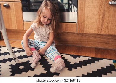cute toddler girl dressing herself at home, wearing pajama and socks