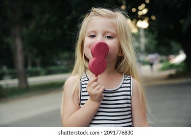 Cute toddler girl eating pink popsicle. Candid outdoor portrait of child with ice cream.	