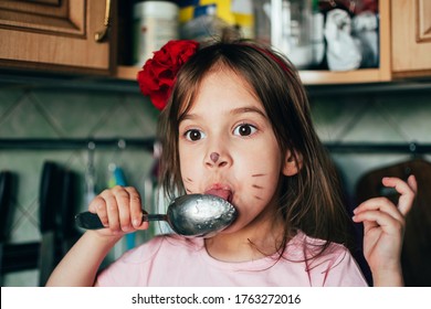Cute  toddler girl with face painting like a cat, licking spoon with honey in the kitchen. Real life moments.  Fun in the kitchen with  little helper.
