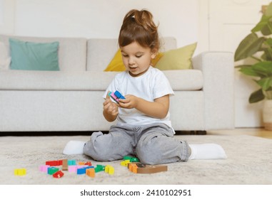 Cute toddler girl playing with colorful blocks while sitting on floor at home, carefully selecting toys, constructing her imaginative world on living room, having fun alone, copy space - Powered by Shutterstock