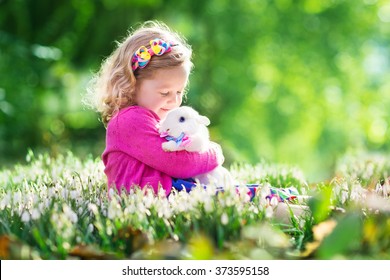 Cute Toddler Girl Playing With Real Rabbit In Blooming Spring Garden. Child On Easter Egg Hunt. Kid With Colorful Eggs And Pet Bunny. Kids Play With Pets. Children Feeding Animal. Family With Animals.