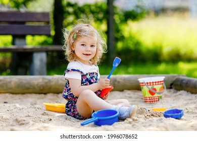 Cute toddler girl playing in sand on outdoor playground. Beautiful baby in red trousers having fun on sunny warm summer day. Child with colorful sand toys. Healthy active baby outdoors plays games - Powered by Shutterstock