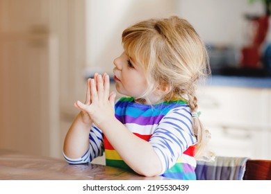 Cute Toddler Girl Praying To God At Home. Child Using Hands For Pray And Thank For Food. Christian Tradition.