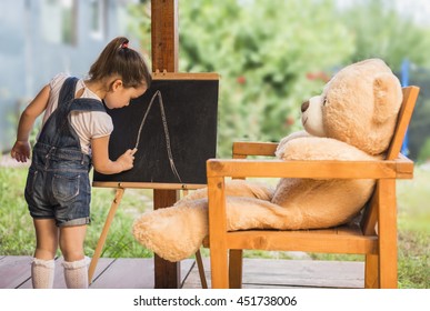  Cute Toddler Playing Teacher Role Game Outdoors. Little Child Drawing With Pieces Of Chalk On A Blackboard. Happy Kid Leaning Letters And Numbers. Children Education Concept