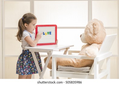 Cute Toddler Playing Teacher Role Game With Her Toy. Happy Little Girl Holding Magnetic Board With Colored Magnetic Letters Written 