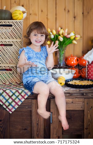 Cute toddler smiling kid in the rustic kitchen indoors. Baking sweet apple cake and having fun. Flour dirty hands, apples, eggs and backing dish. Homemade food.