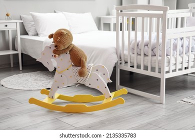 Cute Toy Bear Sitting On Rocking Horse Near Crib In Bedroom